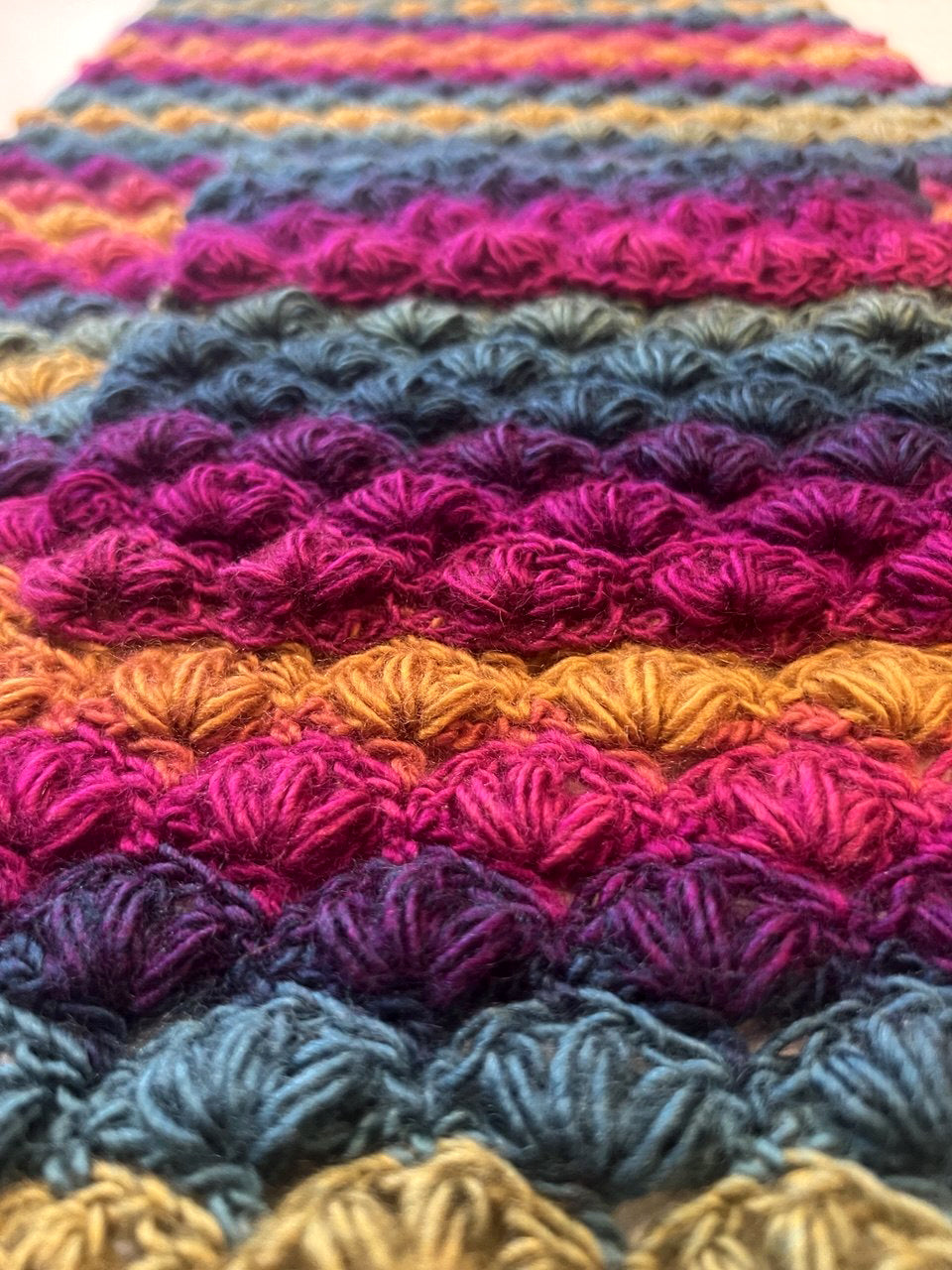 A close-up of a crocheted puff stitch pattern  of Venezia pocket shawl in blue, purple, magenta, orange, and yellow.
